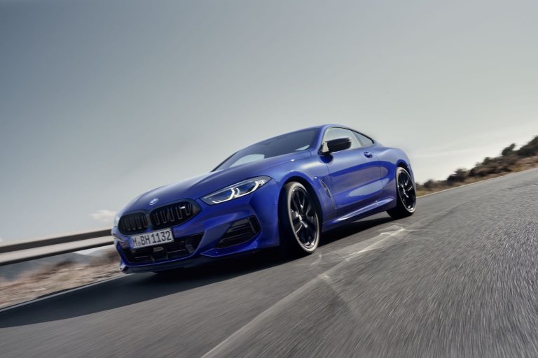 Front view of 2026 BMW 8 Series Coupe in Frozen Portimao Blue driving along coastal highway